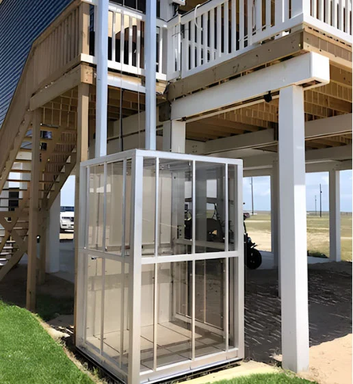 Outdoor home elevator beside a raised house with wooden stairs, providing accessible entry to upper levels.