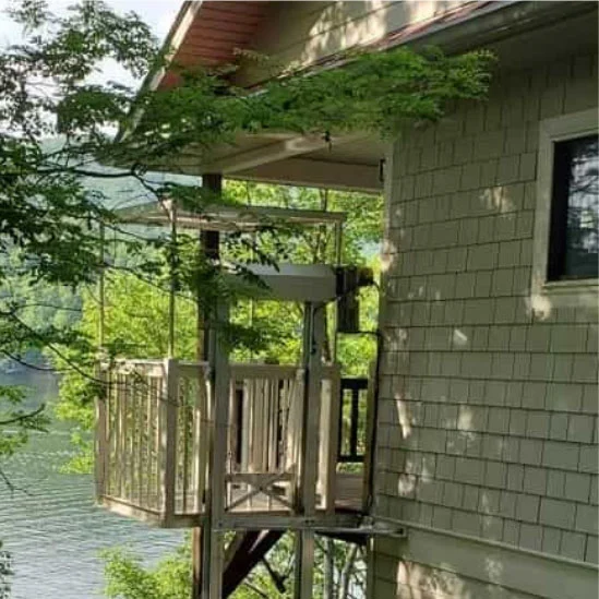 Home elevator attached to a lakeside house, surrounded by greenery, provides access to different levels of the building.