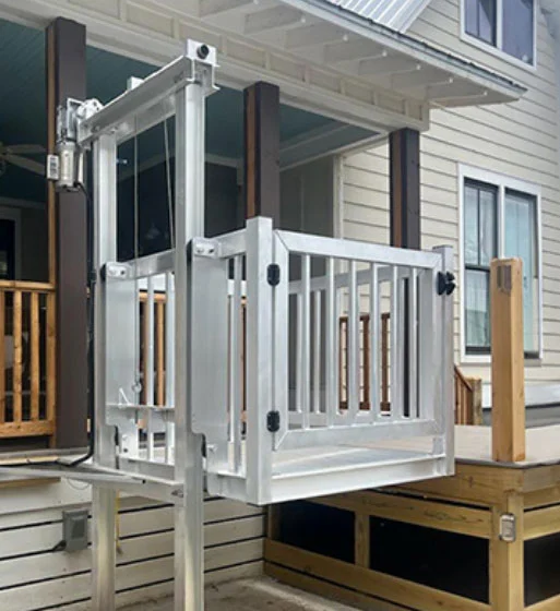 Outdoor home elevator with a metallic frame, situated by a porch, providing accessibility to a raised entryway.